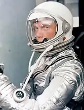 Glenn in a silver spacesuit, with his helmet on and clear visor down