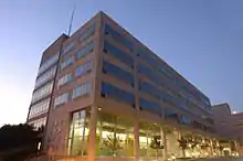 A six-story building of concrete and glass, as viewed from the front corner, with 14th Street parallel to the left face of the building. There are evenly spaced trees in front of the right face of the building.