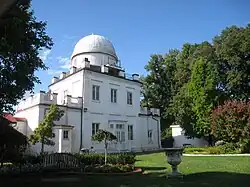 A white square building with a large rusty dome and red accents in winter, with snow on the ground and in trees