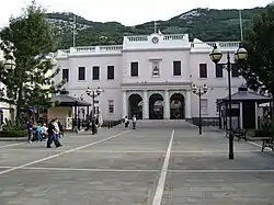 A long plaza with a large two—storey pink building at the far end, with a flight of steps leading up to the building's triple—arched entrance framed with columns.