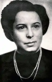 Woman with short, dark hair and dark clothing, accented with a necklace