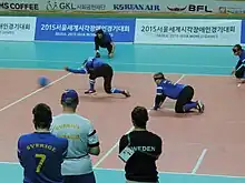 The moment after a Sweden player throws the ball, his arm is still extended as the ball crosses the high ball line. Behind him, a defender is ready on hands and knees to intercept a return ball.