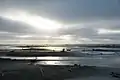 Sandy beach with sunbeams peeking through overcast sky