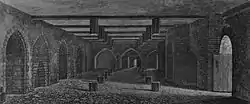 A monochrome illustration of a stone and brick-walled room. An open doorway is to the right. The left wall contains equally spaced arches. The right wall is dominated by a large brick arch. Three arches form the third wall, in the distance. The floor and ceiling is interrupted by regularly spaced hexagonal wooden posts. The ceiling is spaced by wooden beams.