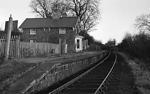 A black and white image of a single platform and single line with a stone built house on the platform