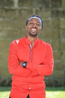 Hannington Bugingo wearing a bright red shirt, arms crossed, laughing while looking at camera