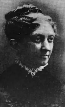 A white woman with wavy hair in an updo, wearing a high lace-trimmed collar