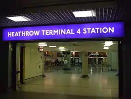 The dark interior of a building with a rectangular, blue sign reading "HEATHROW TERMINAL 4 STATION" in white letters and white flooring