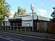 A brown-bricked building with a rectangular, dark blue sign reading "ICKENHAM STATION" in white letters all under a light blue sky