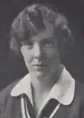 A young white woman with short hair, wearing a rounded collar shirt and a sweater with a deep-v neckline