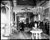 The interior of a home with several people gathered, but wearing winter coats.  Ornate decorative features such as chandeliers and fancy rugs are visible