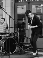 A local band, Interstate Traffic, performs outside the Morris Performing Arts Center in downtown South Bend as part of the "South By South Bend" music festival. Pictured are two members playing a drum set and an electric guitar.