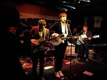 Three musicans standing in a row and performing on a dimly lit stage.