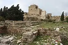 Image of ancient ruins with cypress trees and a fortified castle in the background