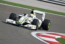 a white and fluorescent green Formula One car drives around a corner