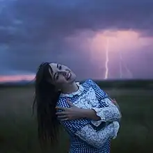 A photo of Williamson smiling and posing in front of a lightning strike in a field