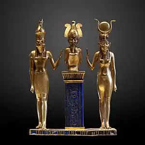 Gold statuette of three human figures. On the right is a woman with a horned headdress, in the center is a squatting man with a tall crown on a pedestal, and on the left is a man with the head of a falcon.