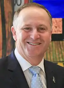 Head and shoulders of a smiling man in a dark suit and pale blue spotted tie