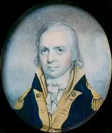 A man with stringy, gray hair wearing a navy jacket with gold epaulets and collar and a high-collared white shirt gathered at the neck