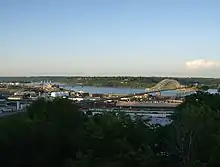 An overlook of a city in the foreground and a river running through the middle of the picture. Three bridges cross the river.