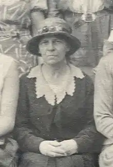 Black and white photograph of seated woman wearing hat and decorative collar.