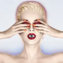 Katy Perry with blonde short hair. She covers her eyes with her hands; an eyeball is visible inside her mouth as her lips are slightly parted.