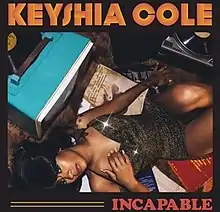 A photograph of Keyshia Cole laying down on a hardwood floor with two record players in front of her.