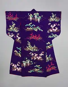 A bright purple kimono viewed from the back, with medium-length sleeves with round edges. The kimono is lined in scarlet and is decorated with embroidery; the design on the sleeves is cut off at the bottom, suggesting they may have been longer at one point. The embroidered design shows different types of flowers and plants on rafts of bamboo tied together with long, waving red cords.