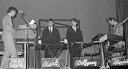 A black and white photograph of four members of Kraftwerk onstage, each with a synthesizer