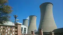 3 enormous waisted vertical concrete cylinders, one emitting a wisp of steam, dwarf a building in the foreground (from Sustainable energy)