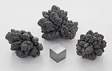 Three, dark broccoli shaped clumps of oxidised lead with grossly distended buds, and a cube of lead which has a dull silvery appearance.