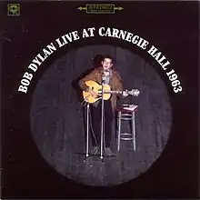 Dylan sitting onstage in front of a microphone playing guitar