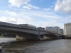 Wide bridge over water against a grey sky with tall buildings