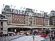 A grey building with three rectangular, white signs reading "London Victoria Station" in black letters all under a clear, white sky