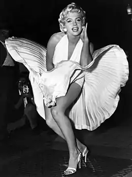 Monroe is posing for photographers, wearing a white halterneck dress, whose hem is blown up by air from a subway grate on which she is standing.