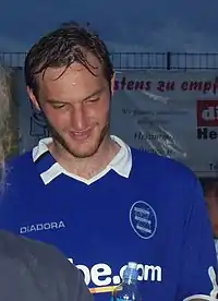 A man in his 20s, wearing a blue shirt with white trim.