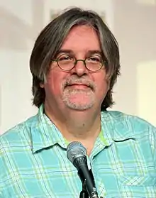 A man in glasses and a plaid shirt sits in front of a microphone.