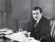 A black-and-white photo of a man sitting behind his desk and reviewing some documents