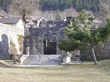 Color photograph of an old building in the background of a grassy area.