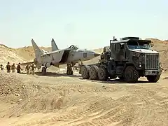 An Iraqi MiG-25RB Foxbat-B found buried under the sand west of Baghdad is towed by an M1070A0