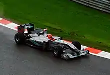 A silver Formula One car with sponsors logo being driven by a man in a red helmet on a race circuit