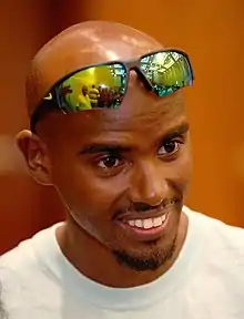 Mo Farah with a white t-shirt and tinted sunglasses on his head.