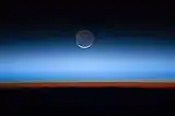 This image shows the Moon at the centre, with the limb of Earth near the bottom transitioning into the orange-colored troposphere. The troposphere ends abruptly at the tropopause, which appears in the image as the sharp boundary between the orange- and blue-colored atmosphere. The silvery-blue noctilucent clouds extend far above Earth's troposphere.