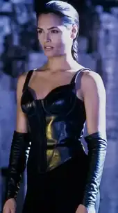 This image shows a black-haired woman with braided hair, wearing an all-black outfit with a corset top, pants and elbows-long handless gloves.