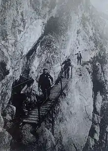 Early photograph with three men about to cross a footbridge.