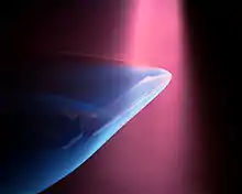 A violet beam from above produces a blue glow about a Space shuttle model