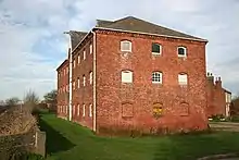 Three-story red brick warehouse built for the Canal company. Slate roof, white painted window frames and gabled hoist door on third floor.