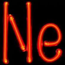 Photograph of glass tube that's been bent to form the connected letters "Ne". The tube is glowing brightly with a red color.