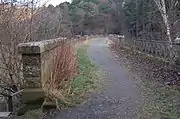 Between the parapet wall on the left and the cast iron railings on the right, a footpath where once there were rails extends across the viaduct, curving gently towards the right and the tunnel mouth