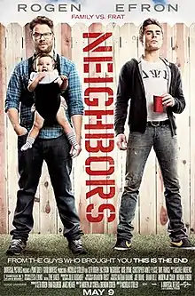 Seth Rogen carrying a baby, standing beside Zac Efron holding a beer, in front of a picket fence.